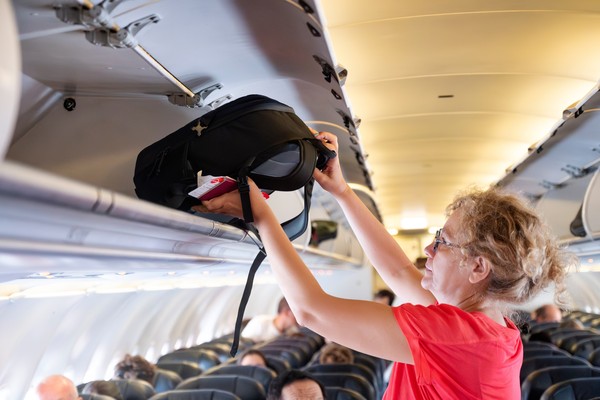 Mujer adulta colocando mochila en el compartimiento superior del avión.
