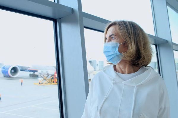 mujer adulta con mascara protectora parada en la ventana de un aeropuerto