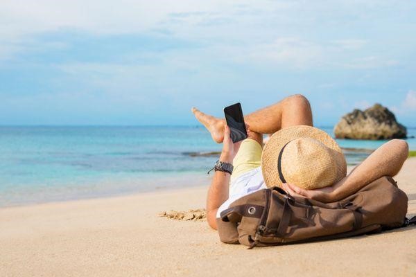 Chico con smartphone tumbado en la playa
