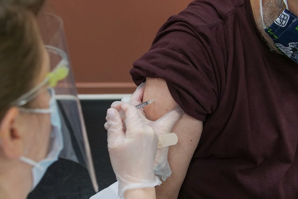 Enfermeira aplicando vacina no braço direito de um homem de terceira idade.