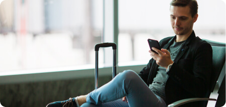 Um homem sentado em um terminal de aeroporto, olhando para o telefone