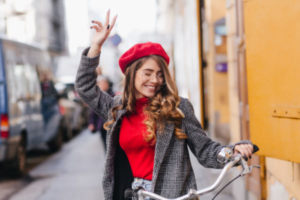 Joven sonriente con boina roja paseando en bicicleta por una calle de Ámsterdam.