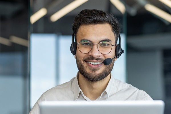Representante masculino de atención al cliente con auriculares y micrófono sonriendo a la cámara en una oficina.