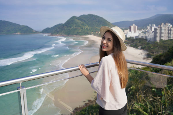 Mujer sonriente con sombrero disfrutando de una vista a la playa y el mar, a salvo gracias a la asistencia al viajero para Brasil.