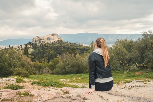 Mujer sentada admirando la Acrópolis, una de los sitios que ver en Atenas.
