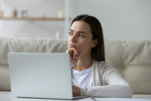 Mujer joven con expresión reflexiva frente a su computadora.