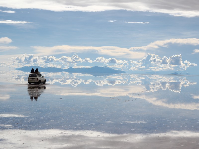 Turistas sobre uma caminhonete atravessando a superfície branca do Salar de Uyuni durante o pôr do sol, em um dos cenários mais emblemáticos da Bolívia.