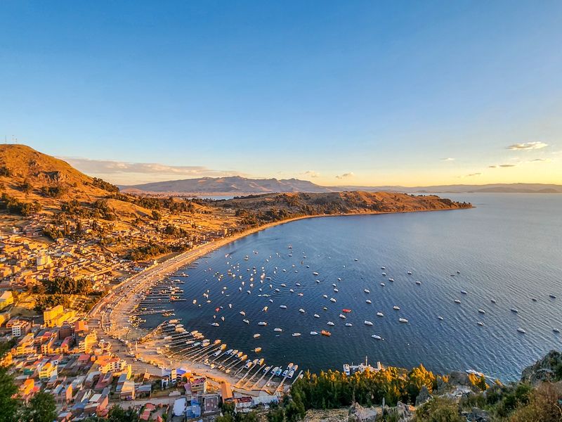 Vista panorâmica do Lago Titicaca com barcos tradicionais e montanhas andinas ao fundo, próximo à cidade de Copacabana, na Bolívia.