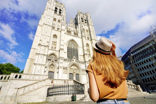 Mujer turista con sombrero mirando hacia arriba la fachada frontal de la Catedral de Bruselas en un día soleado.