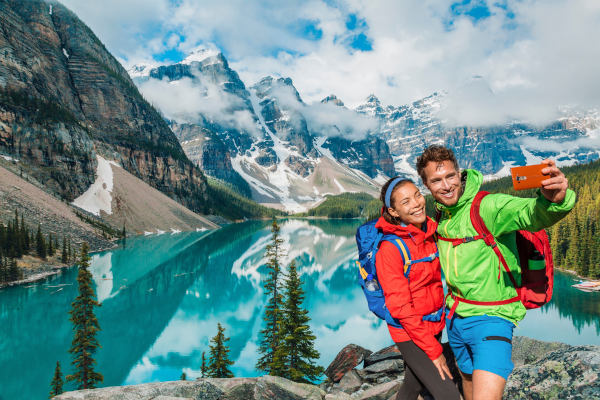Turistas en pareja toman una foto selfie sobre el aumento de viajes en Canadá usando el teléfono.