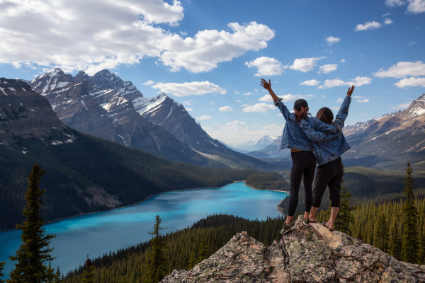 Dos amigas turistas abrazadas sobre una roca celebrando la vista de las Rockies canadienses frente al lago Peyto, Parque Nacional Banff, Alberta, Canadá