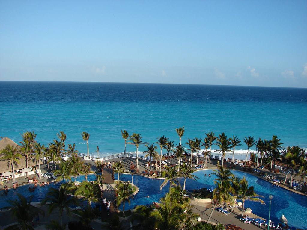 Vista panorâmica de resort à beira-mar em Cancún, com piscinas, coqueiros e o mar azul ao fundo, ilustrando o destino paradisíaco para quem busca saber se Cancún precisa de passaporte.