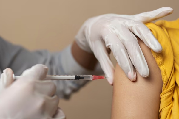 Garota sorridente de camiseta amarela sendo vacinada.  
                    