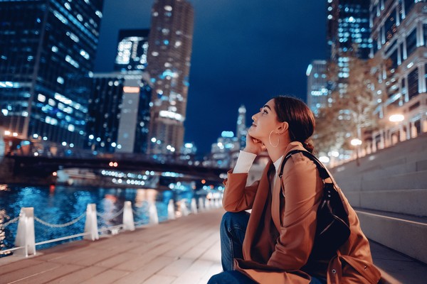Mujer joven contemplando los edificios desde unas escalinatas con vistas al río Chicago en una zona bien iluminada de la ciudad por la noche.