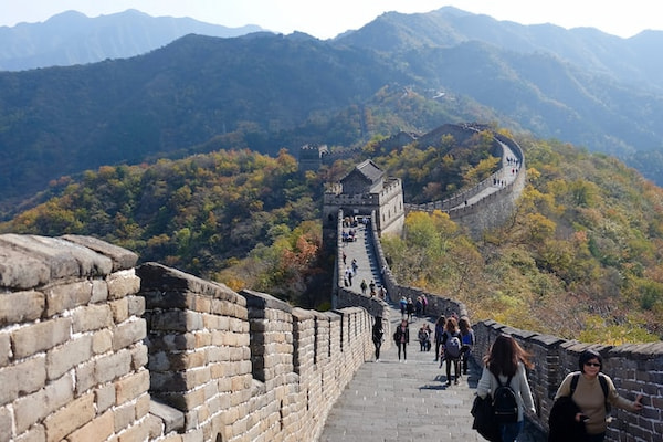 Visão ampla sobre trecho turístico da Muralha da China, com formações rochosas ao fundo.