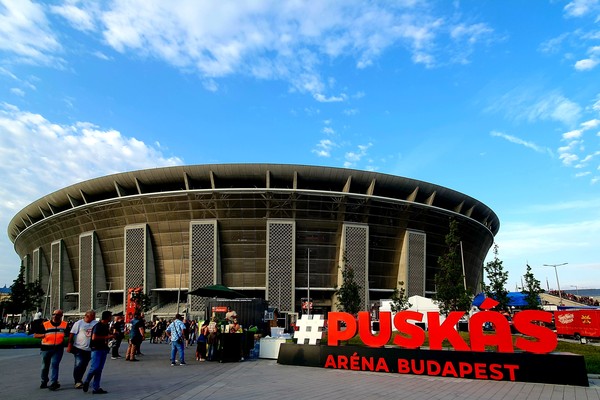 Vista frontal del Puskas Arena de Budapest en un día soleado con gente alrededor.