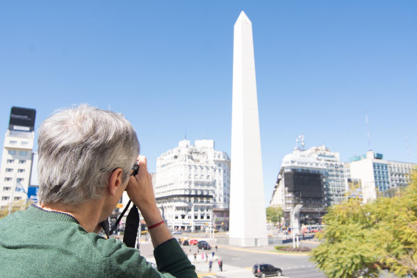 Turista con mochila para bebé feliz en el barrio de La Boca, Buenos Aires, con colorido edificio de fondo.