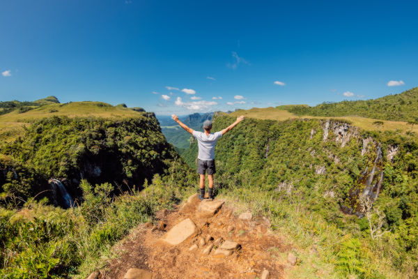 Persona de espaldas con los brazos en alto sobre un acantilado verde en Brasil.