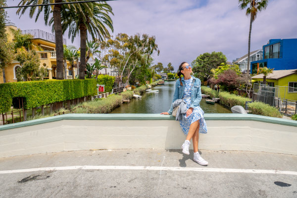 Mujer turista disfrutando del sol sentada en la barandilla de un puente en un canal del barrio de Venice, Los Ángeles.