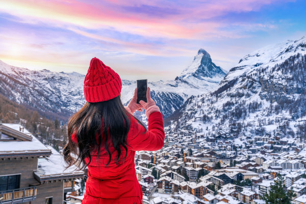 Mujer turista vestida de rojo tomando fotografía desde un lugar con vista panorámica del Monte Cervino y los Alpes en Zermatt, Suiza, en invierno.