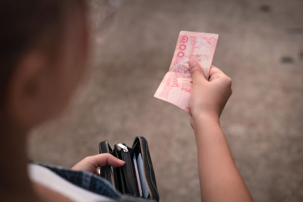 Mujer turista sosteniendo y mirando billete de 100 bahts, la moneda oficial de Tailandia.
