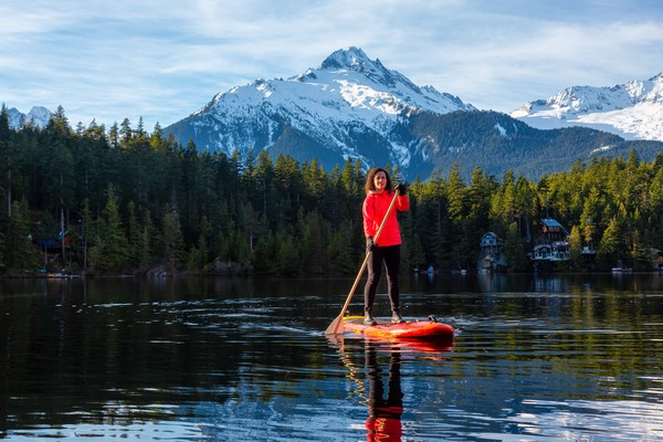 Mujer haciendo paddle board en el lago Levette con arboleda y la famosa sierra Naveda Tantalus en el fondo, Columbia Británica, Canadá.