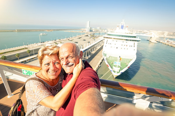 Pareja de adultos mayores tomándose una selfie con un crucero de fondo