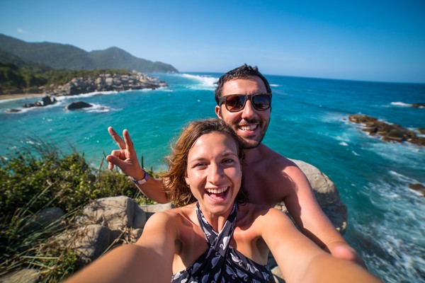 Pareja feliz tomándose una selfie sobre una roca en el Parque Nacional Tayrona, Colombia, con el mar de fondo