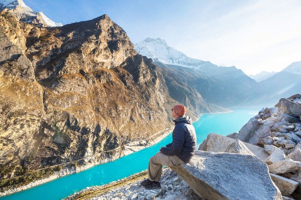 Hombre sentado en una roca con vistas a montañas de la Cordillera de los Andes en Perú.