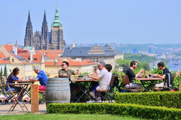 Gente comiendo en mesas exteriores de un restaurante con vistas al Monasterio de Strahov, Praga, República Checa.