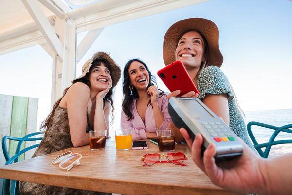 Turistas en bar de playa abonando sus consumos con el celular