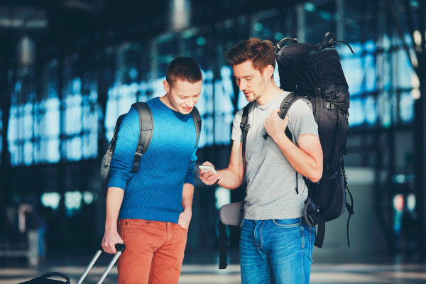 Dos amigos viajeros con equipaje en un aeropuerto mirando un teléfono móvil.