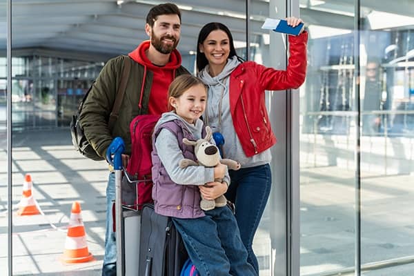 Casal com uma menina pequena no aeroporto sorrindo enquanto seguram suas malas e passaportes