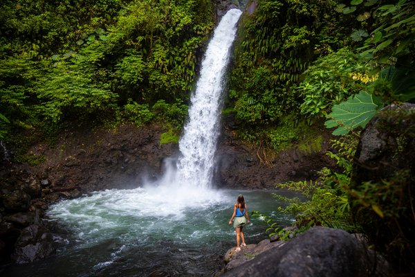 Mujer turista parada en las rocas alrededor de la caída de una cascada en la selva de Costa Rica