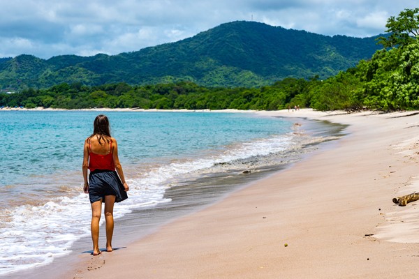 Mujer joven caminando por la famosa playa de Conchal en la costa pacífica de Costa Rica con colinas verdes de fondo.