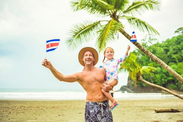 Un hombre con la bandera de Costa Rica riendo con su hija en brazos en una playa de Costa Rica.