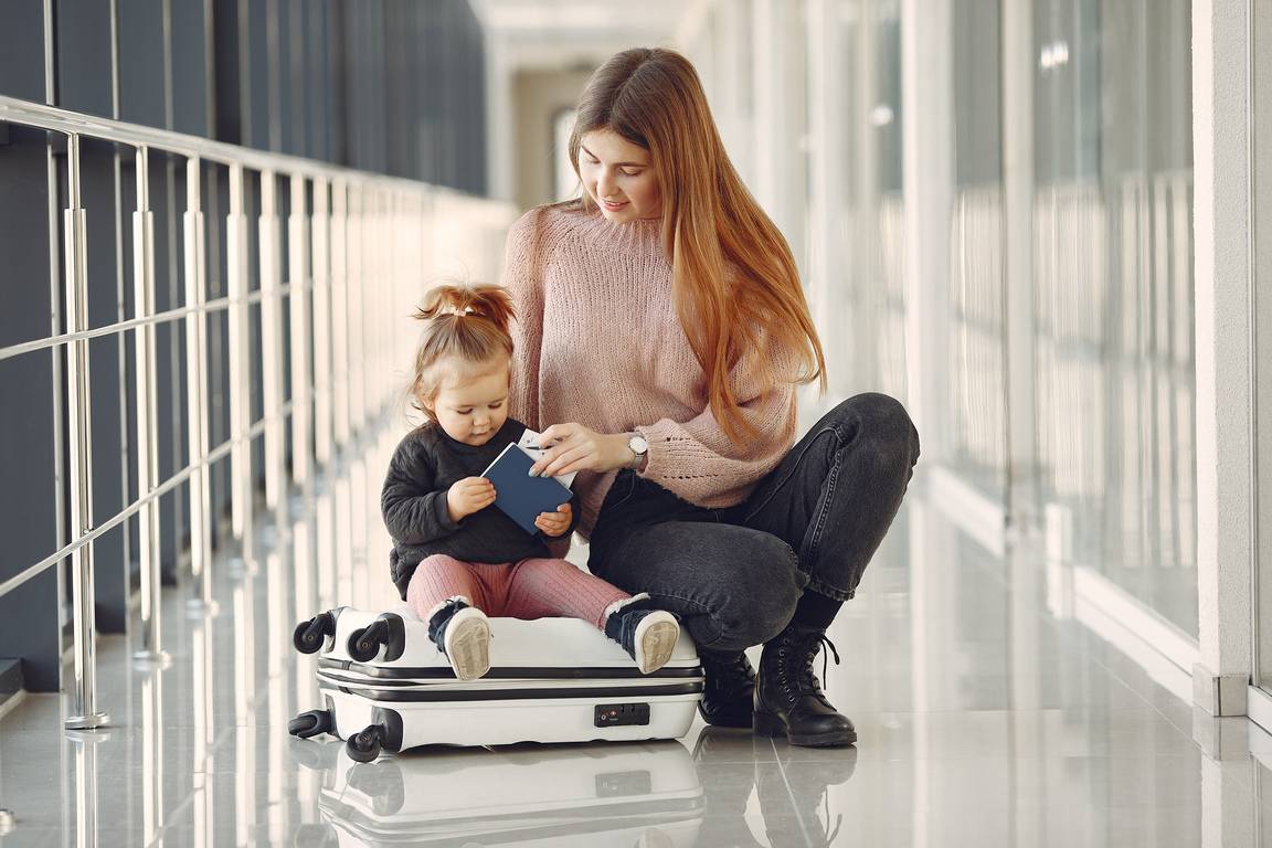 Imagem de mulher com criança segurando um passaporte em aeroporto, em artigo de blog que responde à dúvida comum sobre crianças pagarem passagem de avião em voos nacionais e internacionais