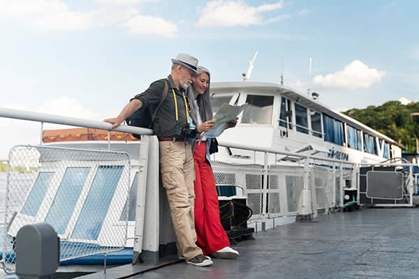 Casal olhando um mapa em frente a um barco representando seguro viagem para cruzeiros