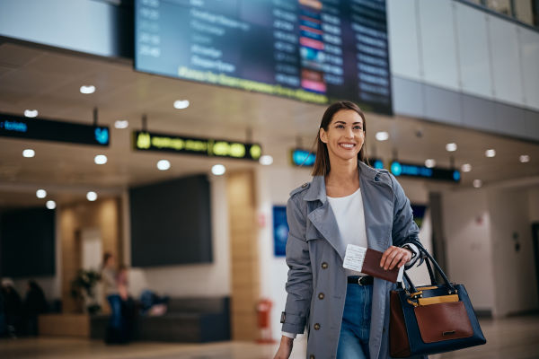 Mujer viajera feliz, con su pasaporte en mano, caminando por un aeropuerto.