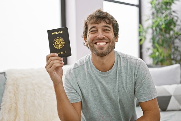 Hombre mostrando pasaporte mexicano en el living de su casa con una sonrisa.