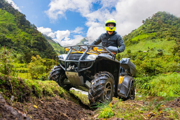 Joven conduciendo cuatrimoto en sendero de montaña rodeado de vegetación verde.