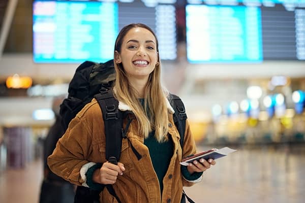 Imagem de mulher com mochila nas costas e segurando passaporte sorrindo