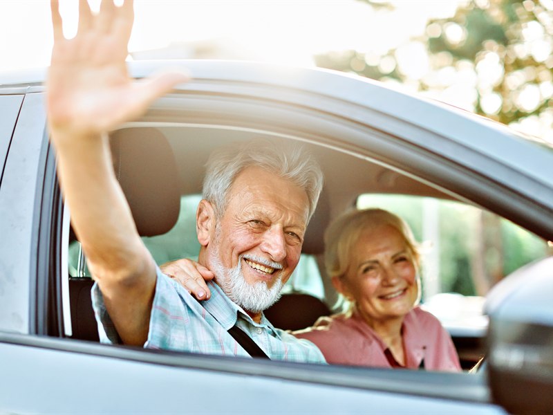 Casal de idosos sorrindo dentro de um carro, prontos para viajar ao exterior com a Permissão Internacional para Dirigir e a CNH brasileira.