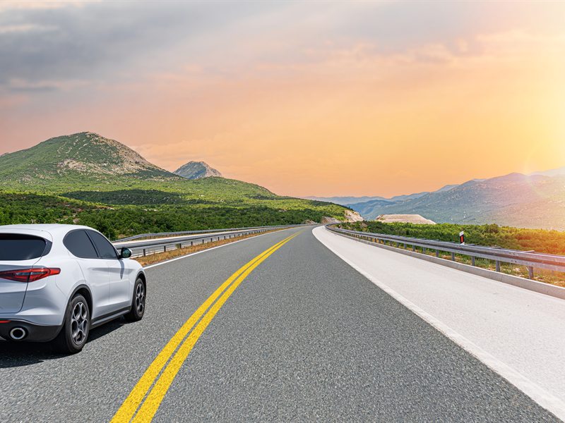Carro em uma estrada aberta com paisagem natural ao fundo, representando uma viagem internacional ao volante com a Permissão Internacional para Dirigir.
