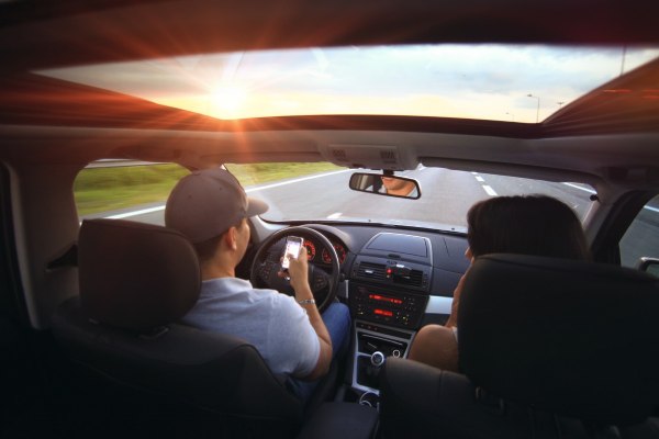 imagem de pessoas dirigindo em estrada para falar sobre dirigir nos eua. Motorista tem um celular nas mãos