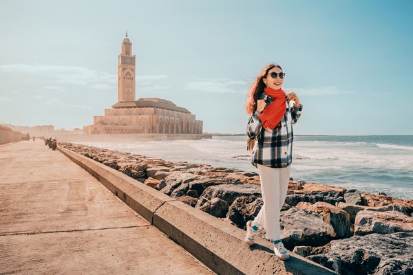 Mujer joven caminando en el rompeolas cerca de la mezquita Hassan II en Casablanca, Marruecos, durante un día soleado.