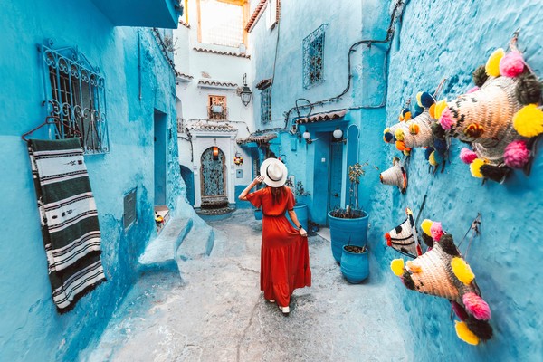 Mujer con vestido rojo y sombrero en una callejuela azul de Chefchaouen, Marruecos.