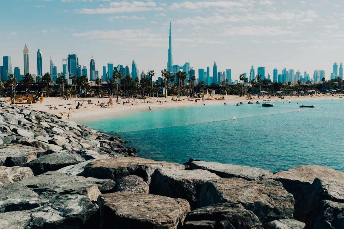 Mulher caminhando na praia com o Burj Al Arab ao fundo, símbolo de luxo entre as atrações de o que fazer em Dubai