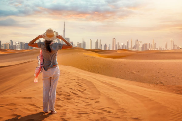 Una mujer turista parada en el Desierto Rojo mirando el horizonte distante de la ciudad de Dubai, Emiratos Árabes Unidos.
