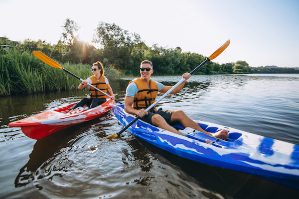 Casal sorridente praticando canoagem em um lago com vegetação nas margens.